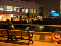 A man checks his phone as he sits by himself near the Central Piers. In the background, the M+ museum's facade can be seen, in Hong Kong, Ch...