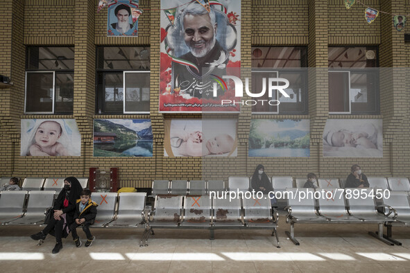 Social distancing signs are pictured on the chairs as mothers and their kids sit under a huge portrait of the former commander of the Islami...