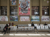 Social distancing signs are pictured on the chairs as mothers and their kids sit under a huge portrait of the former commander of the Islami...