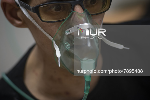 An Iranian man who is infected by COVID-19 uses oxygen while sitting on a hospital bed at a COVID-19 ward in a hospital in the holy city of...