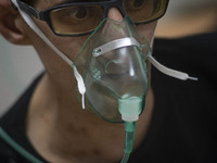 An Iranian man who is infected by COVID-19 uses oxygen while sitting on a hospital bed at a COVID-19 ward in a hospital in the holy city of...