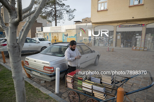 A cleric uses his smartphone while standing next to a cart loaded with religious books on a street-side in the holy city of Qom 145Km (90 mi...