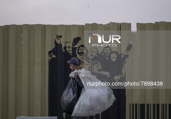 A poor man carrying plastic bags while walking past graffiti on a fence near a holy shrine in the holy city of Qom 145Km (90 miles) south of...