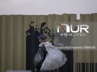 A poor man carrying plastic bags while walking past graffiti on a fence near a holy shrine in the holy city of Qom 145Km (90 miles) south of...