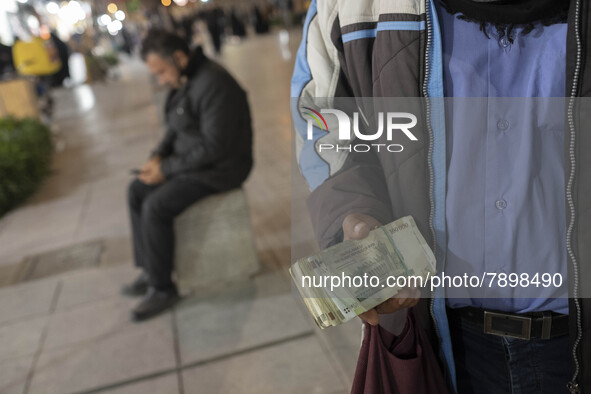 An Iranian street money changer holds Iranian Rial banknotes while standing on a street-side out of a bazaar (Market) near a holy shrine in...