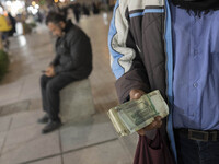 An Iranian street money changer holds Iranian Rial banknotes while standing on a street-side out of a bazaar (Market) near a holy shrine in...