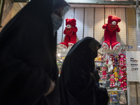 Iranian veiled women walk past two red teddy bears hanged on a wall just out of a toy shop near a holy shrine in the holy city of Qom 145Km...