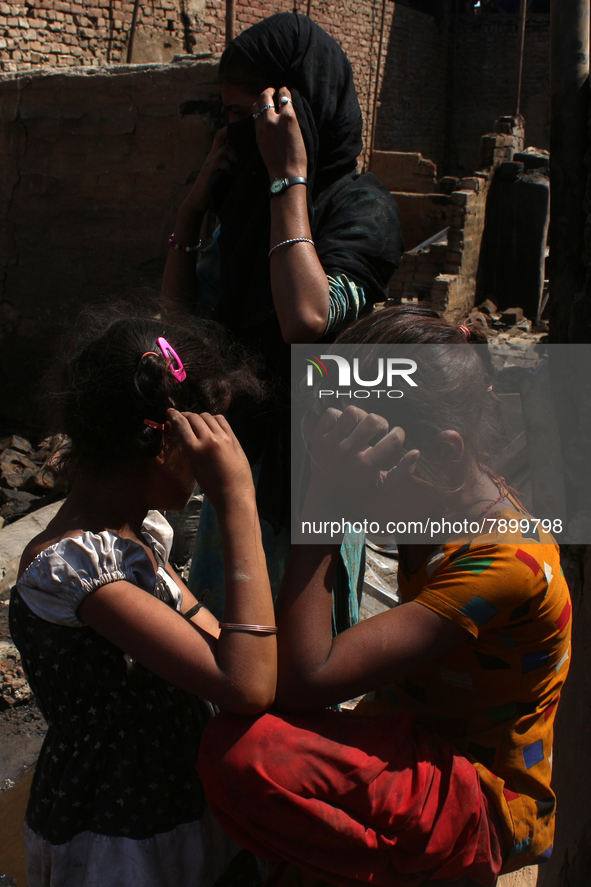 Girls react as they stand outside the charred remains of their home after a fire broke out in a makeshift settlement area around Gokulpuri i...