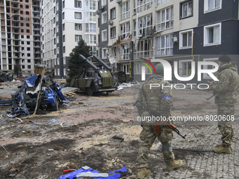 Ukrainian servicemen stands near Destroyed civil vehicles  near a damaged residential building in the recaptured by the Ukrainian army Bucha...