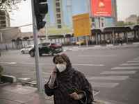 An Iranian woman wearing a protective face mask speaks on her smartphone as she walks along a street-side in Tehran during a polluted air, o...