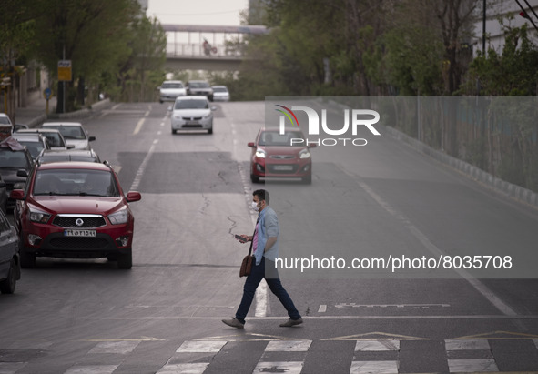 An Iranian man wearing a protective face mask crosses an avenue in Tehran during a polluted air, on April 8, 2022. 