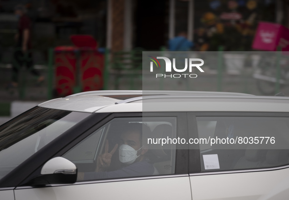 An Iranian driver wearing a protective face mask flashes a Victory sign as a reaction to the camera while driving his vehicle along an avenu...