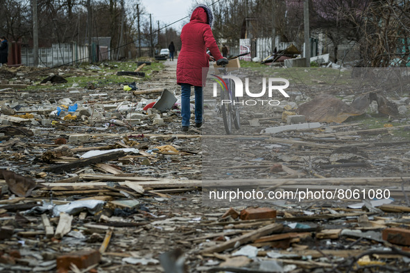 A woman passes with her bicycle over the debris of the destroyed houses by russian shelling in Novoselivka, a village near Chernihiv, Ukrain...