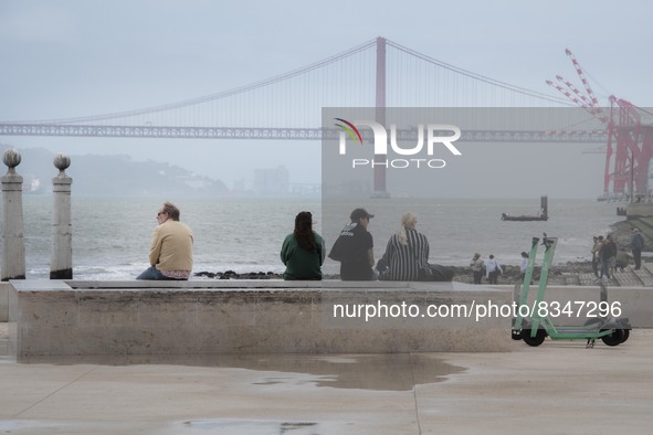 A group of people are seen resting while looking at the 25 April bridge from the Terreiro do Paso area. Lisbon, June 03, 2022. Portugal has...