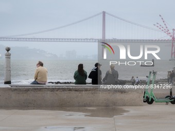 A group of people are seen resting while looking at the 25 April bridge from the Terreiro do Paso area. Lisbon, June 03, 2022. Portugal has...