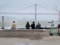 A group of people are seen resting while looking at the 25 April bridge from the Terreiro do Paso area. Lisbon, June 03, 2022. Portugal has...