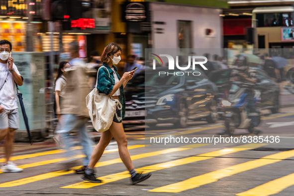 Hong Kong, China, 11 Jun 2022, A masked young lady crosses a street in Mongkok in a panned shot. 