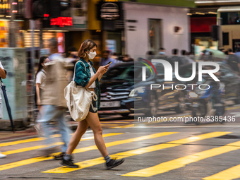 Hong Kong, China, 11 Jun 2022, A masked young lady crosses a street in Mongkok in a panned shot. (