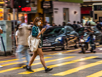 Hong Kong, China, 11 Jun 2022, A masked young lady crosses a street in Mongkok in a panned shot. (