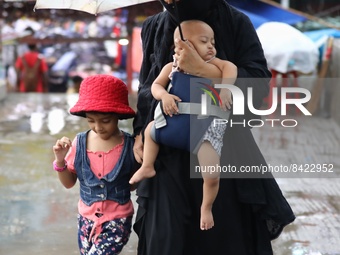 A woman walks thorugh a light rain with her children in Dhaka, Bangladesh on June 17, 2022. (