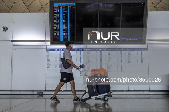 A Man pushing a luggage trolley walk pass an electronic flight display board inside Hong Kong International Airport on July 7, 2022 in Hong...