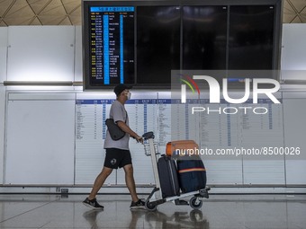 A Man pushing a luggage trolley walk pass an electronic flight display board inside Hong Kong International Airport on July 7, 2022 in Hong...