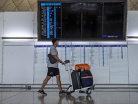 A Man pushing a luggage trolley walk pass an electronic flight display board inside Hong Kong International Airport on July 7, 2022 in Hong...