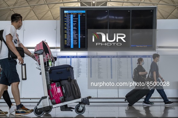 Travellers walk pass an electronic flight display board inside Hong Kong International Airport on July 7, 2022 in Hong Kong, China. The Hong...