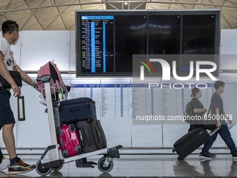 Travellers walk pass an electronic flight display board inside Hong Kong International Airport on July 7, 2022 in Hong Kong, China. The Hong...