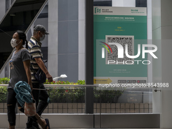 People walk pass a Leave Home Safe QR code placed on a window at the entrance of a shopping mall on July 15, 2022 in Hong Kong, China. (