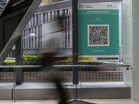 A Long Exposure photo of People walking pass a Leave Home Safe QR code placed on a window at the entrance of a shopping mall on July 15, 202...