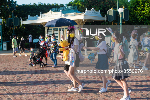 Hong Kong, China, 10 Jul 2022, Young ladies with yellow masks and a Winnie the Pooh plush walk in Hong Kong Disneyland. 