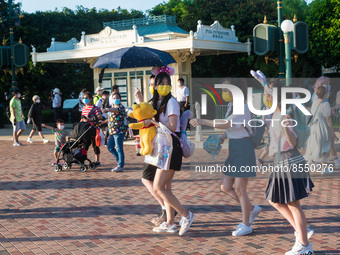 Hong Kong, China, 10 Jul 2022, Young ladies with yellow masks and a Winnie the Pooh plush walk in Hong Kong Disneyland. (