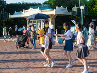 Hong Kong, China, 10 Jul 2022, Young ladies with yellow masks and a Winnie the Pooh plush walk in Hong Kong Disneyland. (