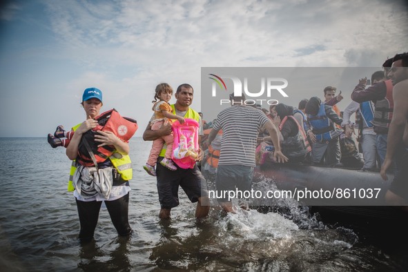 Volunteers help migrants embark from the dinghy they have arrived on, in Lesbos, on September 27, 2015.  