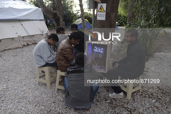 Migrants from Pakistan charge their mobile phones, near the main Police station in Kos Town, as hundreds of new arrived migrants awaiting on...