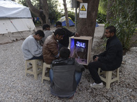 Migrants from Pakistan charge their mobile phones, near the main Police station in Kos Town, as hundreds of new arrived migrants awaiting on...