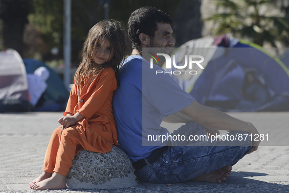 A young Fariba (age 3) from Afganistan sitting with her father in Kos harbour, as her family awaiting to be processed by the Greek police an...