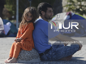 A young Fariba (age 3) from Afganistan sitting with her father in Kos harbour, as her family awaiting to be processed by the Greek police an...