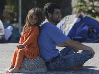 A young Fariba (age 3) from Afganistan sitting with her father in Kos harbour, as her family awaiting to be processed by the Greek police an...