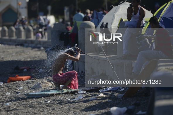 A migrant washes himself in front of the main Police station, as awaiting in Kos harbour to be processed by the Greek police and given paper...