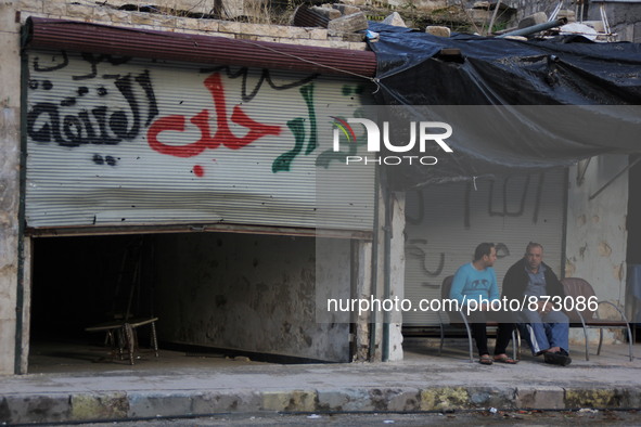 Two of the men sitting beside an advert written on the wall in Aleppo, Syria october 27,2015. The text on the wall reads in Arabic, "old rev...