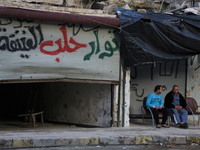 Two of the men sitting beside an advert written on the wall in Aleppo, Syria october 27,2015. The text on the wall reads in Arabic, "old rev...