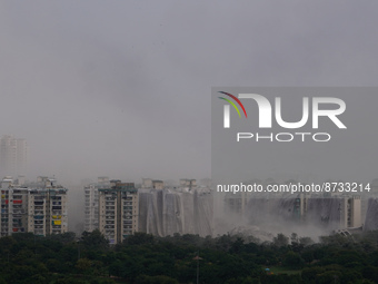 Nearby residential buildings are engulfed by dust as the Supertech Twin Towers collapse following a controlled demolition by explosion after...