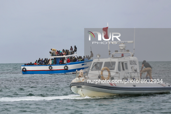 A small sailboat crowded with nearly 118 people and unity of Tunisian guard watch them 