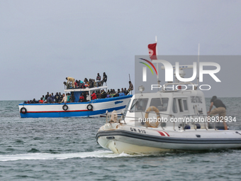 A small sailboat crowded with nearly 118 people and unity of Tunisian guard watch them (