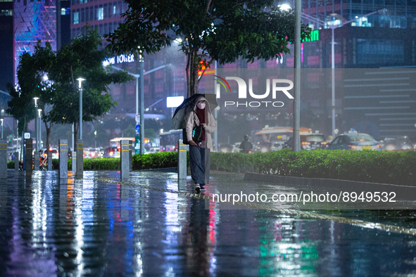 Women with umbrella wear protective face masks walk in business district on the main street in Jakarta on 3 October 2022. President Joko Wid...