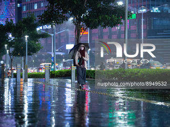 Women with umbrella wear protective face masks walk in business district on the main street in Jakarta on 3 October 2022. President Joko Wid...