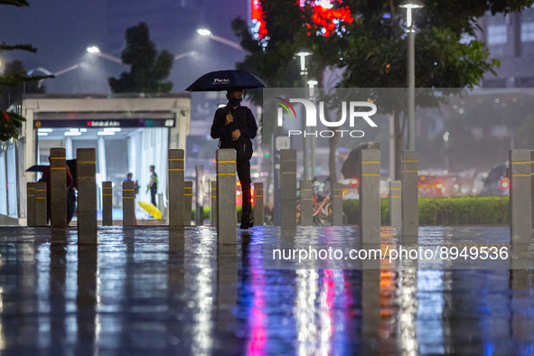 A man with umbrella wear protective face masks walk in business district on the main street in Jakarta on 3 October 2022. President Joko Wid...