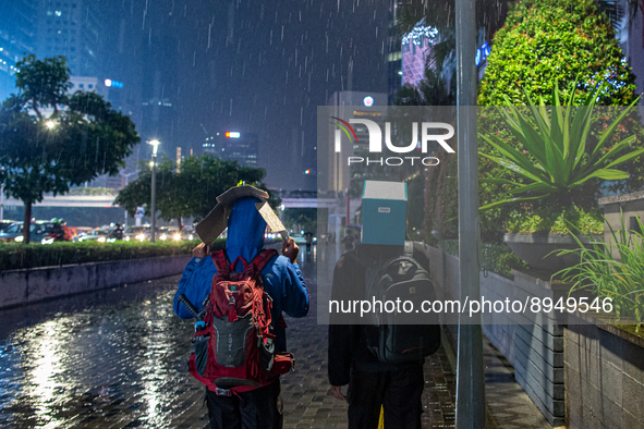 People cover their heads with boxes to avoid the rain  in business district, Jakarta on 3 October 2022. President Joko Widodo mentioned the...